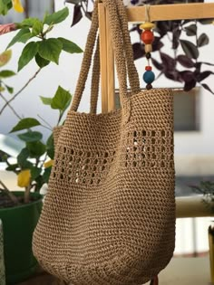 a crocheted bag hanging from a wooden hanger next to potted plants