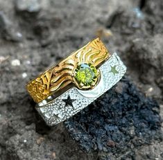 two tone gold and silver ring with green stone in the center on top of rocks