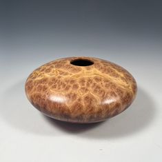 a wooden vase sitting on top of a white table next to a black object with holes in it