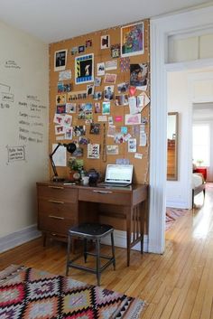 a desk with a laptop on top of it next to a wall covered in pictures