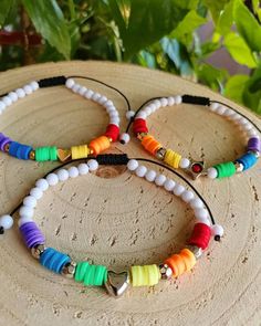 three bracelets with different colored beads on top of a piece of wood next to plants