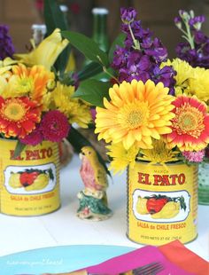 three yellow cans with flowers in them are sitting on a table next to plates and utensils