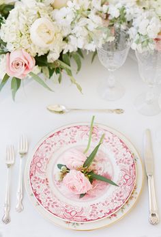 the table is set with pink and white plates, silverware, and floral centerpieces