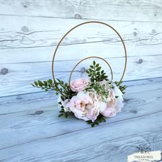 a pink flower arrangement in a gold hoop on a white background with wood planks