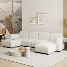 a living room with white furniture and pictures on the wall above the couch, coffee table and stairs