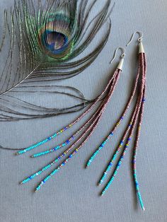 three pairs of peacock feather earrings with beaded ends on a gray surface next to each other