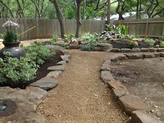 a garden area with rocks, plants and trees in the back yard or fenced off area