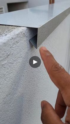 a hand is pointing at the corner of a wall with a metal strip on it