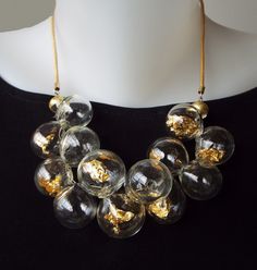 Unique and chic, This Glass beads bib necklace, for sure is a conversation starter. This Clear and Gold bubbles statement necklace combines transparent hollow glass beads, Filled with pieces of 22 karat gold leaf, in a cluster shape, connected to a Leather cord, and closes with a goldfilled clasp. The necklace has 2 inches (5 cm) chain to adjustable length. You can pair this unique necklace with these earrings: https://etsy.me/3Qg86lX This bold-blown airy jewelry is light and easy to wear, Perfe Luxury Adjustable Glass Necklace, Luxury Handmade Clear Necklace, Clear Glass Necklaces For Party, Clear Glass Jewelry For Party, Modern Glass Necklaces For Formal Occasions, Modern Glass Necklaces For Formal Events, Unique Glass Necklace For Parties, Handmade Glass Necklaces In Clear Color, Handmade Glass Clear Necklaces