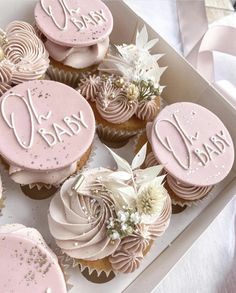 cupcakes decorated with pink frosting and white flowers are in a box on a table