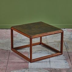 a square wooden table sitting on top of a tiled floor next to a green wall