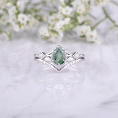 an engagement ring with a green stone surrounded by white flowers