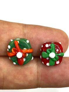 two small red and green christmas decorations sitting on top of a persons finger in front of a white background