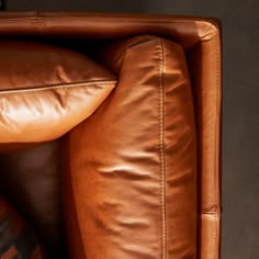 a brown leather couch with two pillows on it's back and one pillow in the middle