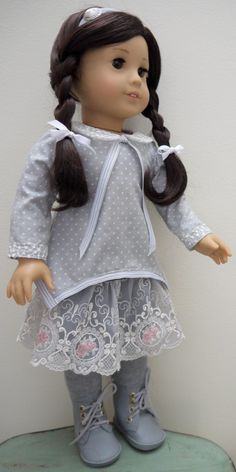 a doll with long brown hair wearing a gray dress