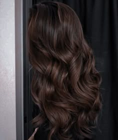 the back of a woman's head with long, wavy brown hair in front of a black curtain