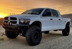 a white truck parked on top of a dirt road next to a mountain at sunset