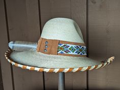 The Jasmine hat starts with a Gus fine palm hat body that is made in Mexico. It has a 4" brim and 5 1/2" crown. Hand laced in saddle color leather lace. The hatband has a layer of saddle tan suede that serves as the background for the beaded strip. The back of the band has 3 mini Conchos. Finished with a "red tail hawk" feather that is created from a turkey feather. Note: Hats are made to order. Allow up to 4 weeks for your hat to ship. Natural Brimmed Hat For Western-themed Events, Natural Hat Bands For Rodeo, Natural Color Hat With Short Brim For Western-themed Events, Brimmed Toquilla Straw Hat For Western-themed Events, Natural Short Brim Hat For Western-themed Events, Curved Brim Straw Hat For Western-themed Events, Natural Hat Band With Flat Brim For Country Events, Adjustable Straw Hat With Flat Crown For Country Events, Handmade Flat Crown Hat Bands For Rodeo