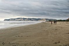 two people are walking on the beach near the water