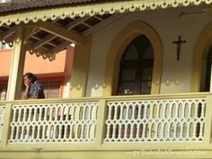 a woman standing on the balcony of a building with an iron cross hanging from it's roof