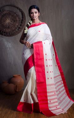 This stunning red and white cotton saree is a traditional Bengali style known as the dhaniakhali saree. Made from high-quality cotton and finished with a stiff starch, this saree is perfect for any formal occasion. The intricate white designs on the red background make for a bold and eye-catching look. Add this saree to your collection for a timeless piece that will never go out of style. Color : Red and Off White .  Blouse Piece : No.  Fall Pico : Yes.  Care : Dry-Clean Only. White Cotton Silk Saree For Puja, White Cotton Silk Traditional Wear For Diwali, White Cutdana Saree For Rituals, White Cotton Saree With Traditional Drape, White Cotton Saree With Zari Work, White Cotton Silk Traditional Wear With Border, White Handloom Saree For Traditional Ceremonies, White Handloom Traditional Wear For Rituals, White Traditional Wear With Zari Weaving For Navratri