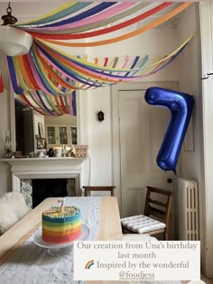 a birthday cake on a table with streamers hanging from the ceiling and an inflatable balloon above it