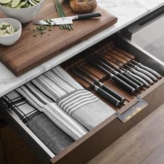 an open drawer with utensils and other kitchen items in it on a marble countertop