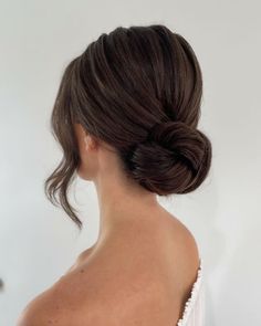 a woman with her hair in a low bun, looking off to the side while wearing a white dress