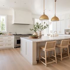 a large kitchen with white cabinets and gold pendant lights hanging from the ceiling over the island