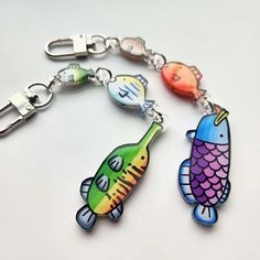 two colorful fish shaped key chains on a white surface, one with metal clasps and the other with plastic clippings