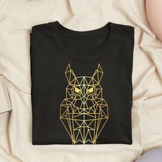 a black t - shirt with gold geometric owl on it's chest and eyes