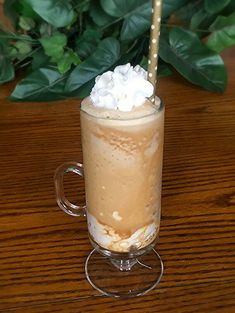 there is a drink with whipped cream in it on the table next to a plant