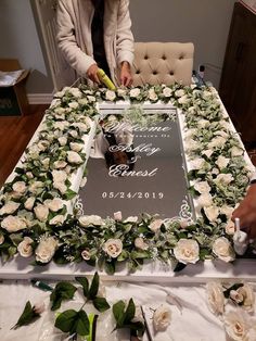 a woman cutting into a large cake with flowers on the table next to her and another person standing behind it