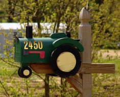 a green tractor mailbox sitting on top of a wooden post in front of some trees