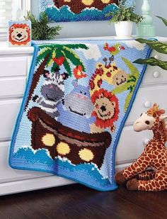 a stuffed giraffe sitting next to a crocheted blanket with animals on it