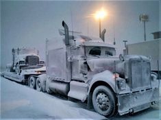 two semi trucks are parked on the side of the road covered in snow at night