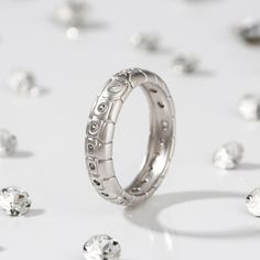 a wedding ring surrounded by diamonds on a white surface with scattered jewels in the background