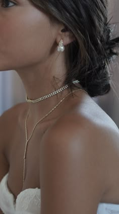 a woman in a white dress wearing a gold necklace and earring with pearls on it