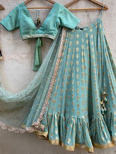 A three-piece ocean green ruffle lehenga set from the Priti Sahni collection. This elegant ocean green butti georgette lehenga with big ruffle detailing and gota border is paired with an ocean green raw silk blouse with sequin, pearl border. The lehenga has side hanging ball tassels to the waistline. And the blouse has a coin-beads tassel tie-up at the back. The outfit is completed with an ocean green sequined butti work dupatta with scalloped edging. Bollywood Style Ruffled Lehenga For Navratri, Festival Designer Anarkali Set With Ruffles, Eid Floor-length Ruffled Lehenga, Festival Anarkali Set With Ruffles, Festive Ruffled Anarkali Set For Designer Wear, Floor-length Ruffled Choli For Festivals, Elegant Green Ruffled Sharara, Transitional Green Lehenga With Gota Work, Festive Floor-length Lehenga With Ruffles