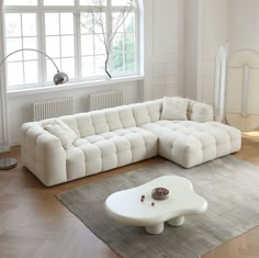 a large white sectional sofa sitting on top of a wooden floor next to a window