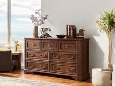 a wooden dresser sitting in front of a window next to a vase with flowers on it