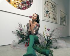 a woman sitting on the ground with flowers in front of her and holding a flower