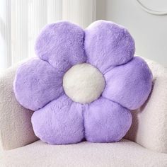 a purple flower shaped pillow sitting on top of a white chair next to a window