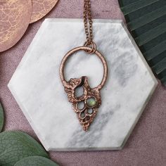 a close up of a necklace on a marble block with leaves and foliage in the background