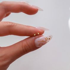 a woman's hand with white and gold manicures on her nails, holding a tiny diamond ring