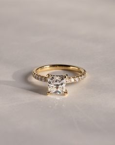 a gold engagement ring with a princess cut diamond on the side and pave set shoulders