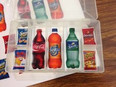 several plastic containers filled with different types of sodas and snacks on a wooden table