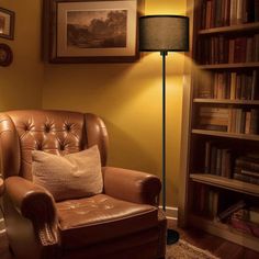 a brown chair sitting in front of a lamp next to a book shelf filled with books