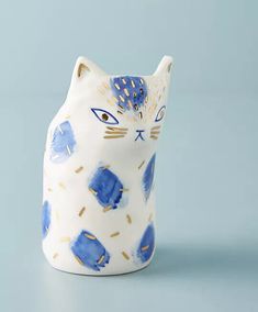 a blue and white cat shaped vase with gold spots on it's face, sitting on a light blue surface