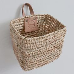 a woven basket hanging on the wall with a leather tag attached to it's handle